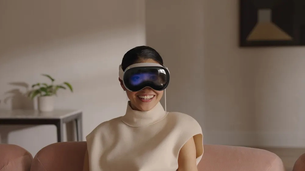 Mulher feliz com headset branco de realidade mista, exibindo olhos digitais azuis na tela, em sofá.