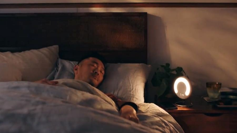 Homem dormindo na cama, luminária de cabeceira acesa.