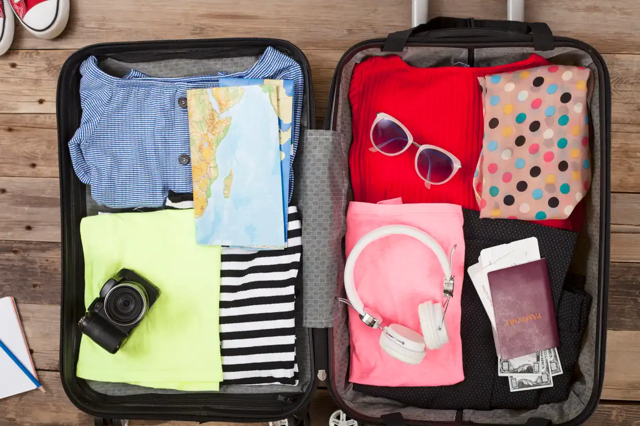Mala de viagem aberta com roupas, câmera, óculos de sol, passaporte, fone de ouvido e dinheiro, pronta para uma viagem