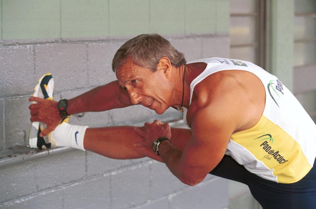 Homem em regata alongando a perna esticada, segurando o pé.
