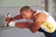 Homem em regata alongando a perna esticada, segurando o pé.