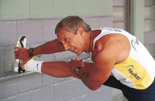 Homem em regata alongando a perna esticada, segurando o pé.