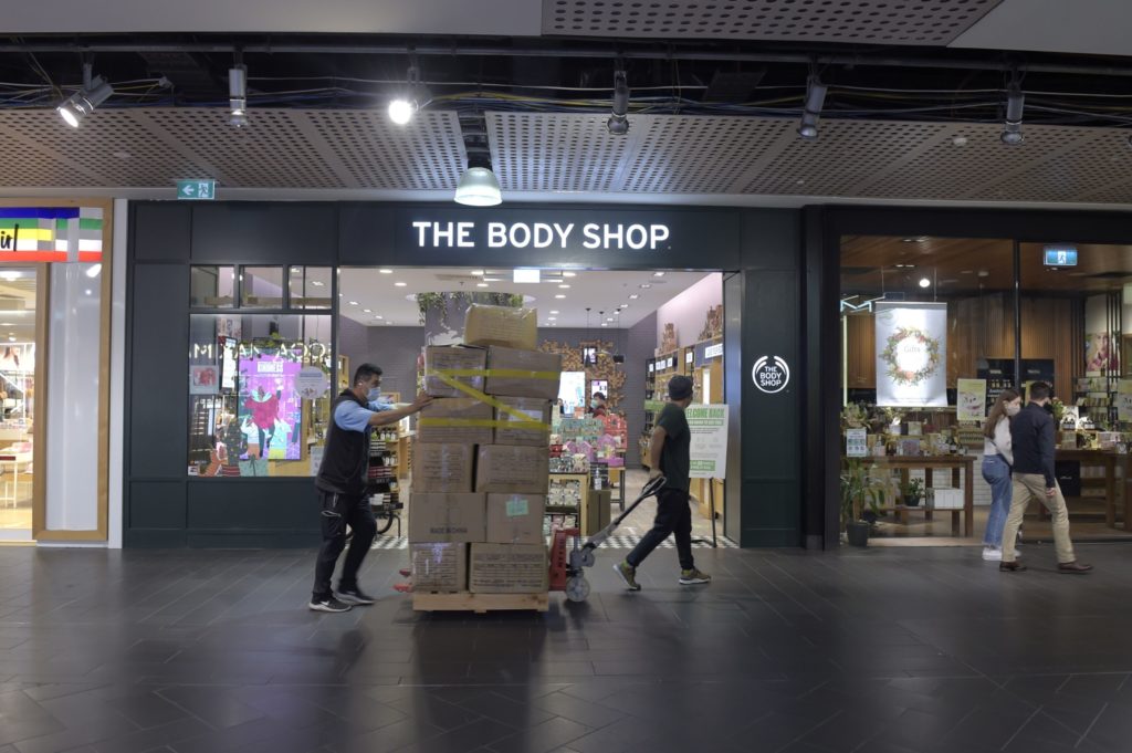 Trabalhadores movimentam caixas em palete no corredor de um shopping, na frente da loja The Body Shop.