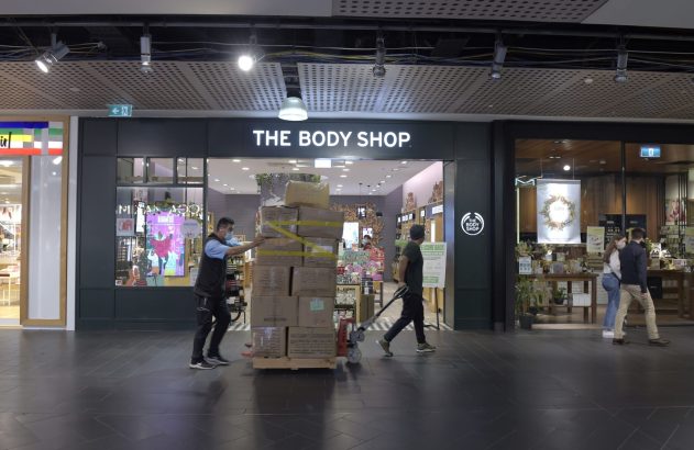 Trabalhadores movimentam caixas em palete no corredor de um shopping, na frente da loja The Body Shop.