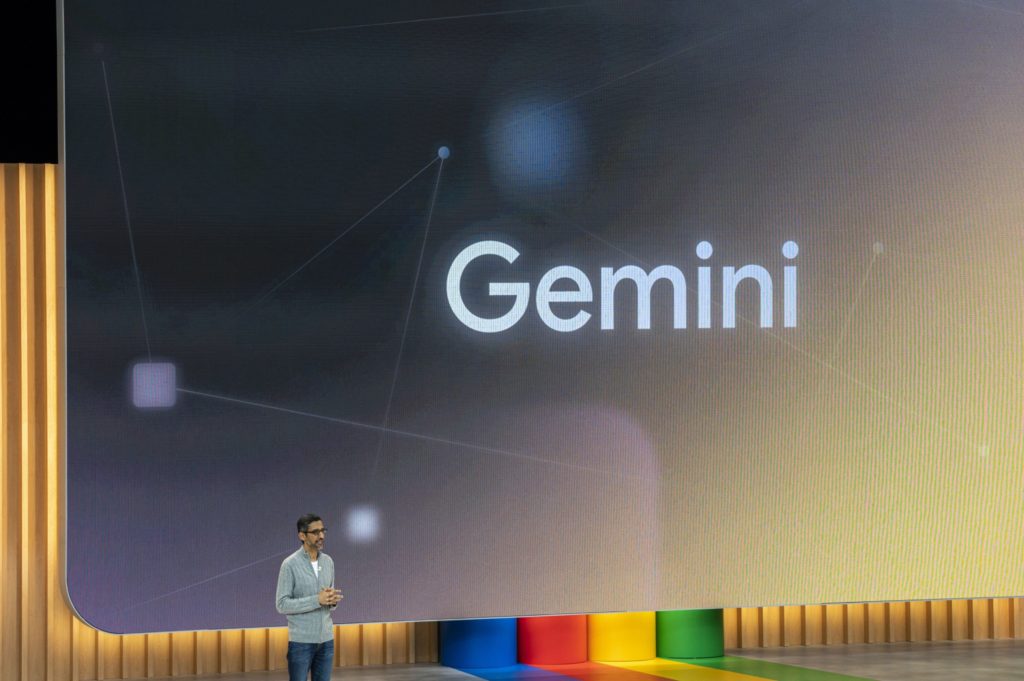 Homem no palco, tela exibe "Gemini" com gráficos abstratos. Apresentação Google.