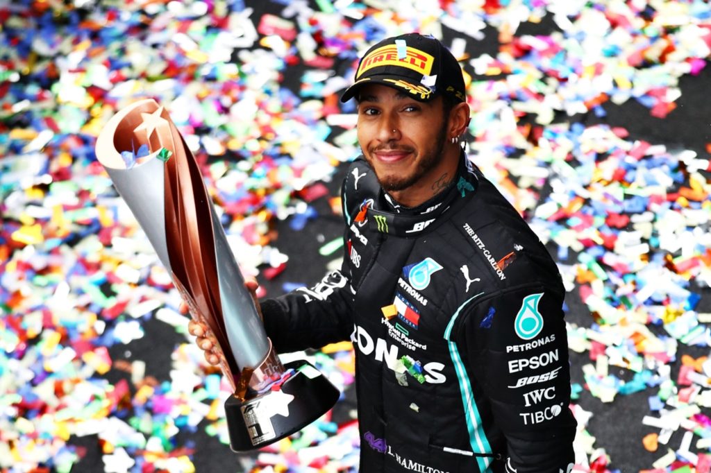 Lewis Hamilton sorrindo, segurando um troféu, em meio a confetes coloridos.