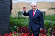 Sebastián Piñera, ex-presidente do Chile, sorrindo e acenando em um jardim com flores vermelhas.