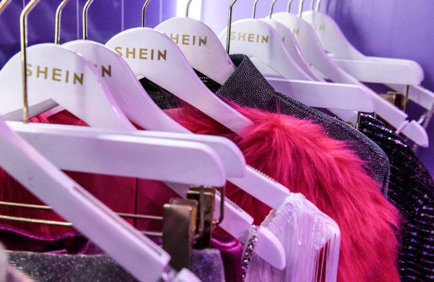 Roupas de diversas cores penduradas em cabides brancos com o logo 'SHEIN' em um expositor.