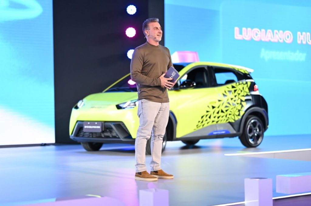 Homem em palco apresenta carro elétrico verde-limão em evento de lançamento.