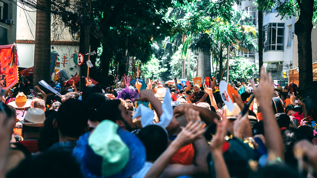 Multidão em rua arborizada, pessoas com mãos levantadas em celebração ao ar livre.
