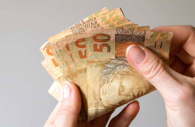 Mãos contando cédulas de 50 Reais.