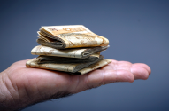 Mão aberta segurando uma pilha de notas de dinheiro dobradas.