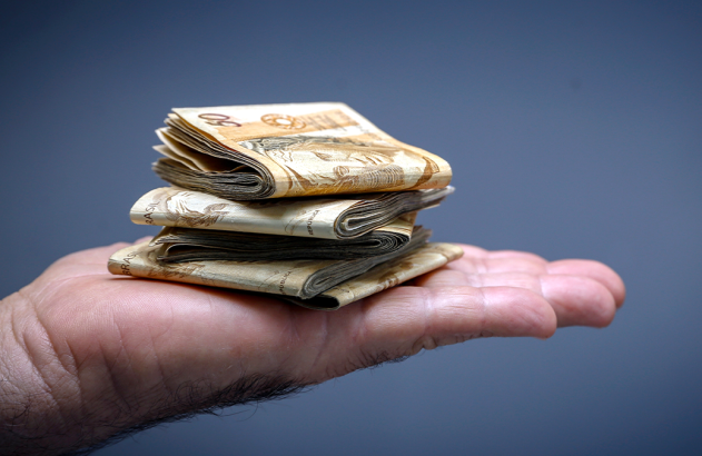 Mão aberta segurando uma pilha de notas de dinheiro dobradas.