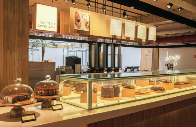 Interior de confeitaria Dengo com vitrine de doces, balcão de atendimento e equipamentos de café.