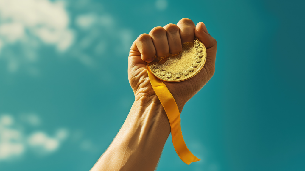 Punho erguido segurando medalha de ouro e fita amarela contra céu azul com nuvens.