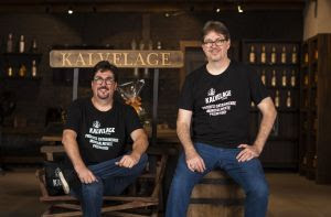 Dois sócios da Kaivelage, em camisetas da marca, posam sorrindo na frente de sua loja.