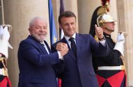 Presidentes Lula e Macron sorriem e apertam as mãos. Macron faz sinal de positivo. Guardas em uniforme de gala atrás.