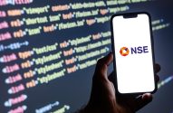 Mão segura smartphone exibindo o logo da NSE, com código de programação digital em segundo plano.