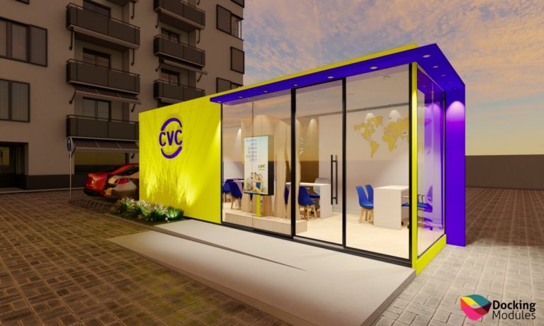 Quiosque modular CVC amarelo e roxo com janelas de vidro, em área externa pavimentada com edifício e carro.