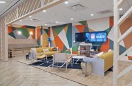 Lounge moderno com mural geométrico colorido, sofás amarelos e TVs exibindo o logo Reddit.