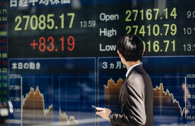 Homem de terno observa grande tela digital com dados e gráficos do mercado de ações.