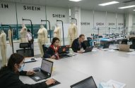 Funcionários Shein em laptops, manequins e máquinas de costura em escritório de design de moda.