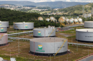 Complexo industrial da Petrobras com tanques de armazenamento e cidade ao fundo.