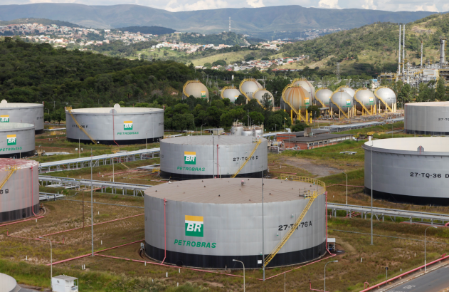 Complexo industrial da Petrobras com tanques de armazenamento e cidade ao fundo.