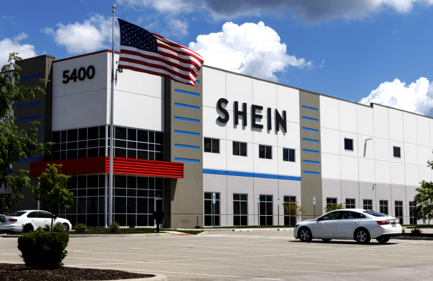 Edifício SHEIN com bandeira dos EUA e carro branco em estacionamento, sob céu azul.