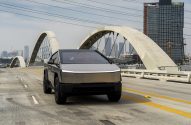 Tesla Cybertruck em ponte de concreto com grandes arcos e skyline urbano. Dia claro.