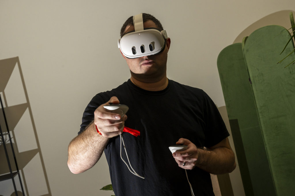 Homem com headset de realidade virtual branco e controles com alça vermelha, jogando.