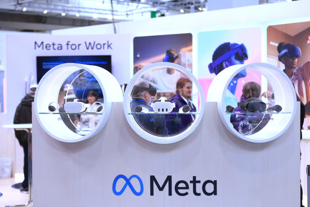 Pessoas interagem com displays circulares em estande da Meta, destacando "Meta for Work".