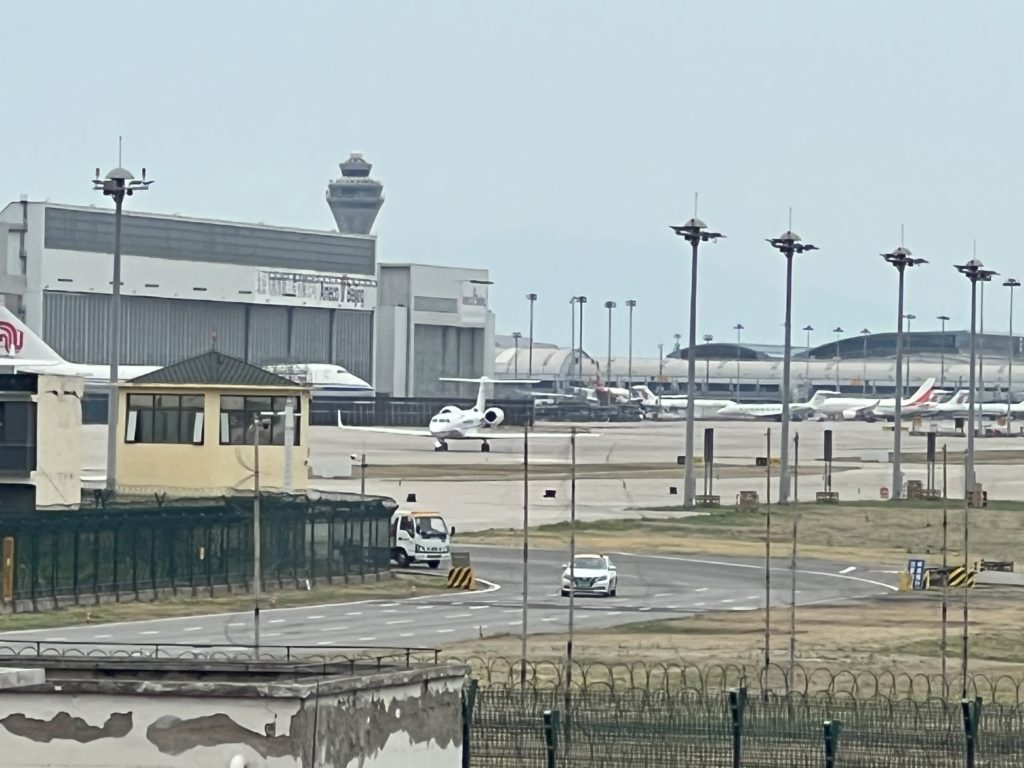 Aeroporto com pátio molhado, torre de controle, aviões e veículos.