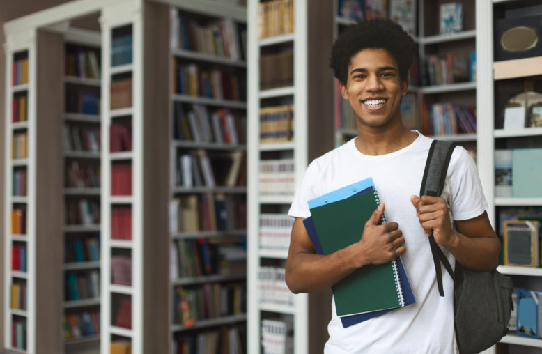 Jovem estudante segurando cadernos em uma biblioteca