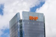 Edifício de vidro com as letras "BHP" em laranja, sob céu com nuvens brancas.