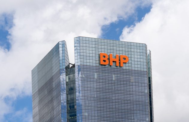 Edifício de vidro com as letras "BHP" em laranja, sob céu com nuvens brancas.