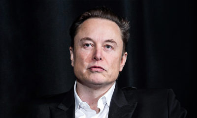 Elon Musk está de paletó preto e camisa branca, olhando para cima