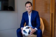 Homem de terno azul sentado, segurando uma bola de futebol.
