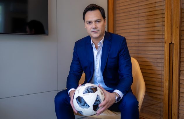 Homem de terno azul sentado, segurando uma bola de futebol.