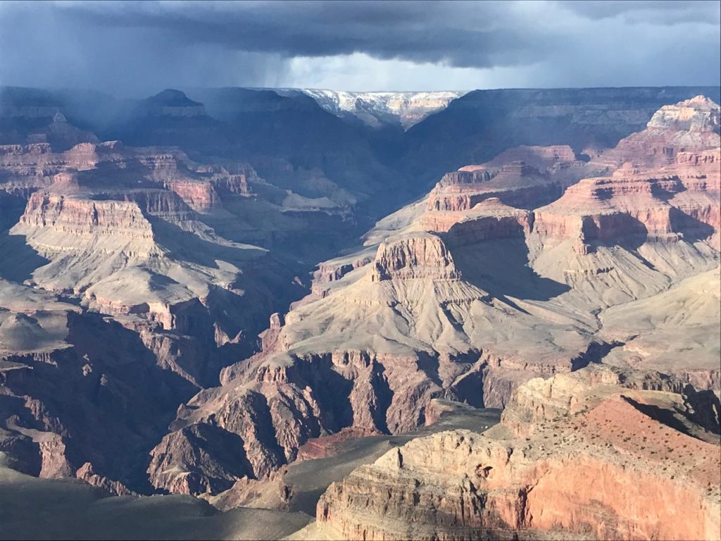 Grand Canyon: vale rochoso com chuva caindo no horizonte sob céu cinzento.