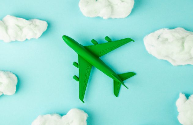 Avião de brinquedo verde voa no céu azul entre nuvens de algodão brancas, vista de cima.