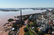 Vista aérea de uma cidade inundada por água barrenta. Prédios e ruas submersos. Barcos próximos a um grande edifício com chaminé.
