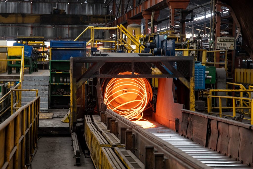 Metal incandescente em espiral sendo transportado por esteira em siderúrgica.