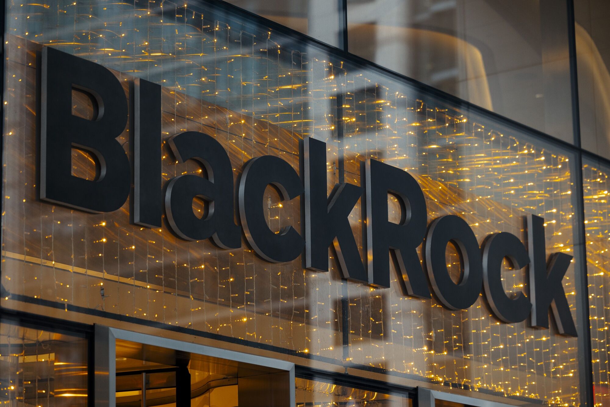 Letreiro "BlackRock" em uma fachada de vidro com luzes amareladas ao fundo.
