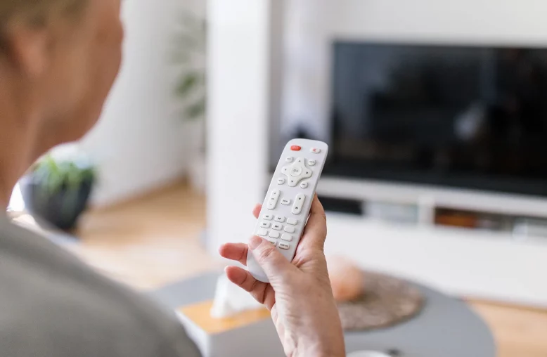 Mulher idosa segurando um controle remoto em frente à TV