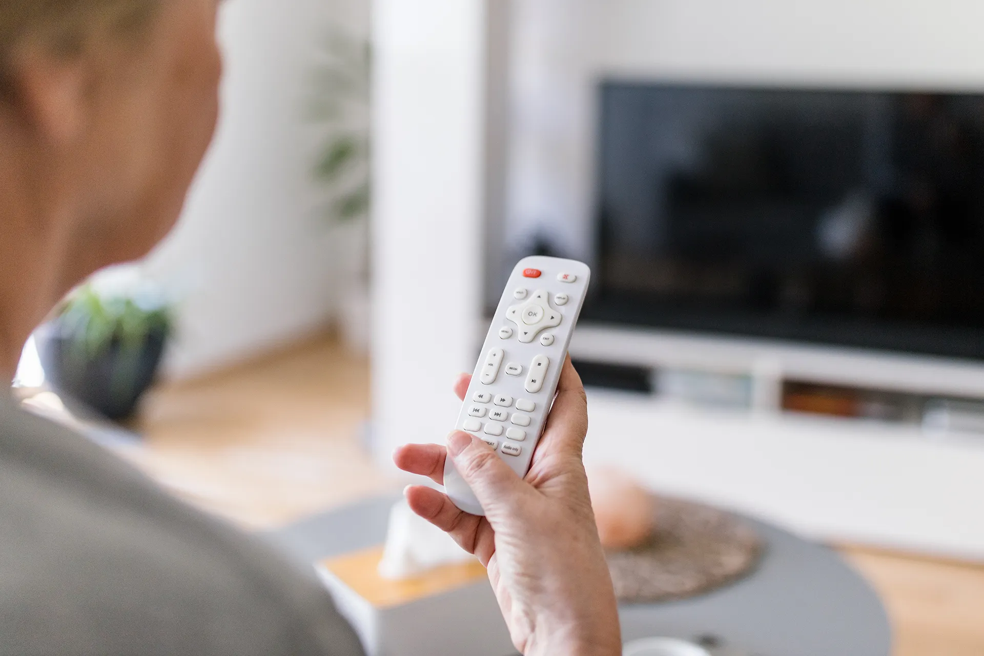 Mulher idosa segurando um controle remoto em frente à TV