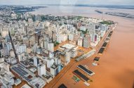Vista aérea de cidade com enchentes severas: prédios e ruas submersos em água barrenta.