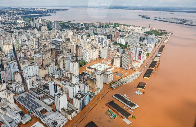 Vista aérea de cidade com enchentes severas: prédios e ruas submersos em água barrenta.