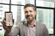 Homem sorridente exibe smartphone com aplicativo de mapa repleto de pontos vermelhos.