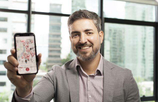 Homem sorridente exibe smartphone com aplicativo de mapa repleto de pontos vermelhos.